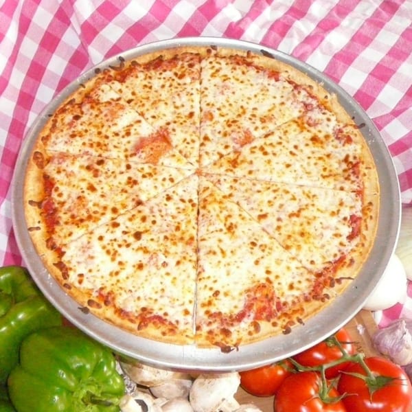 A cheese pizza on a metal pan, surrounded by fresh green bell peppers, mushrooms, and tomatoes.