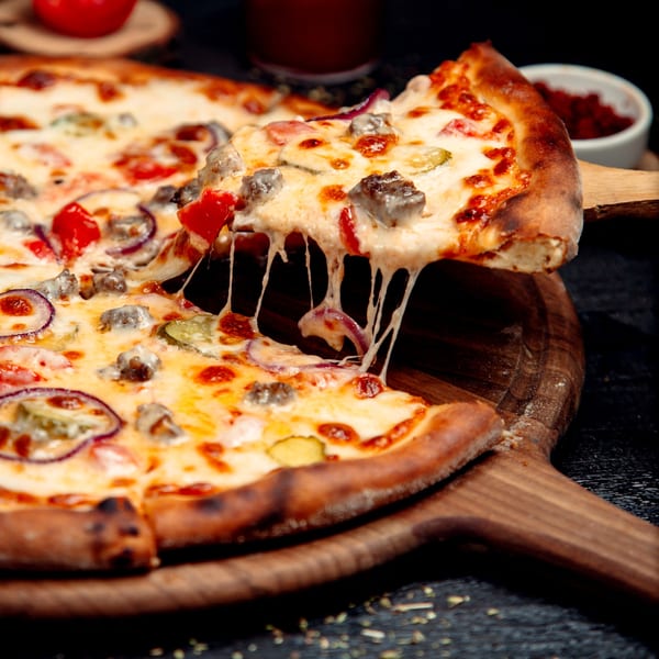 A slice of Pizza King of Irving's pizza with melted cheese, red onions, and meat being lifted.